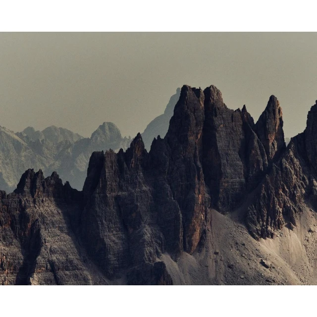 Dramatic mountain range under a hazy sky. Jagged peaks rise with steep rock faces in a landscape photo, showcasing rugged natural beauty.