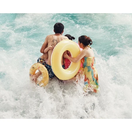 Family with two kids wading into rushing water with inflatable yellow rings. A woman in a dress follows behind them.