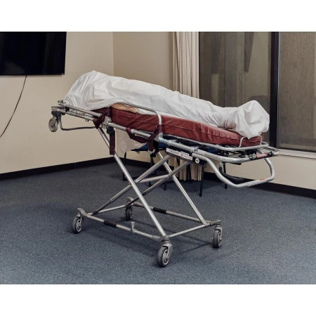 Hospital gurney with white sheet in an indoor medical environment with window and wall-mounted television, reflecting a clinical setting.
