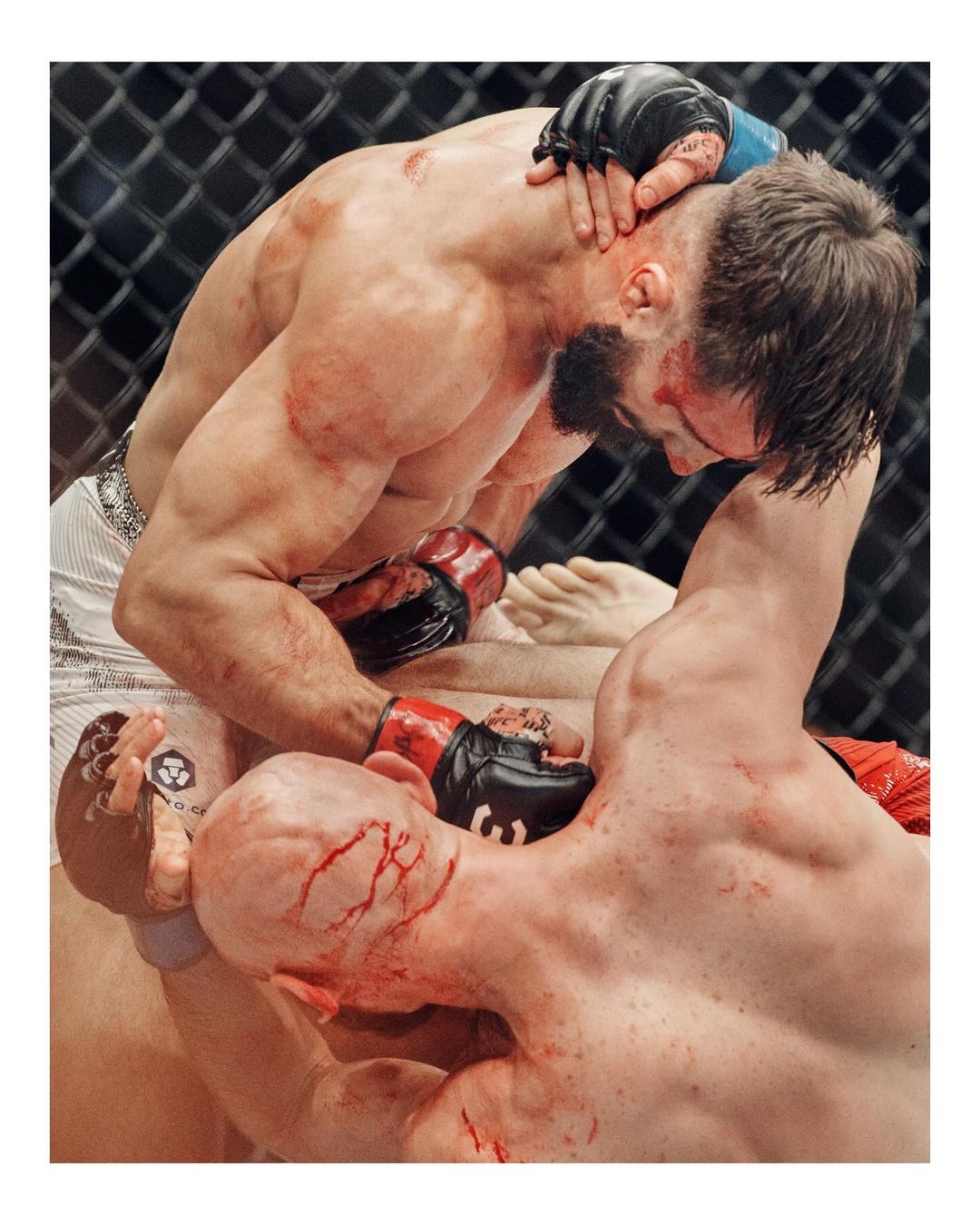 Two male athletes wrestling in an indoor arena with visible signs of blood and physical exertion, showcasing a raw and intense moment of competition.