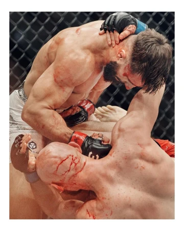 Two male athletes wrestling in an indoor arena with visible signs of blood and physical exertion, showcasing a raw and intense moment of competition.