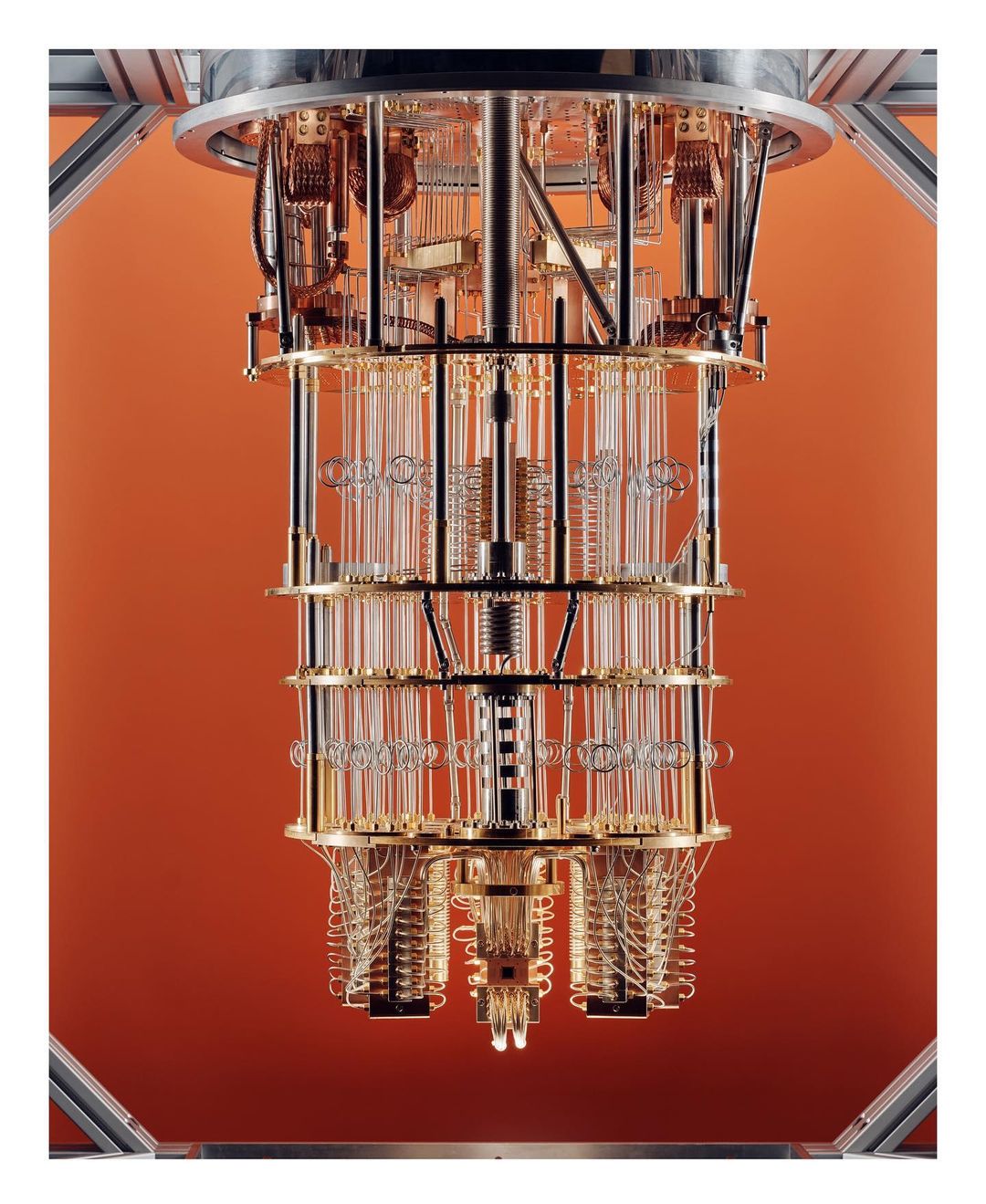 A large, complex scientific apparatus featuring glass tubes and metal components set against a solid orange background, showcasing technology.