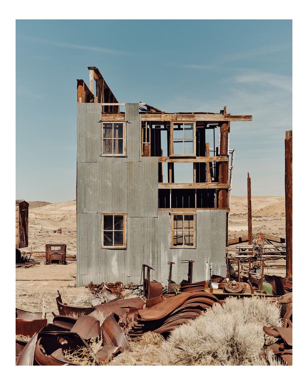 Exterior view of a dilapidated, corrugated metal building with missing sections under a blue sky in a desert environment with rusty metal.