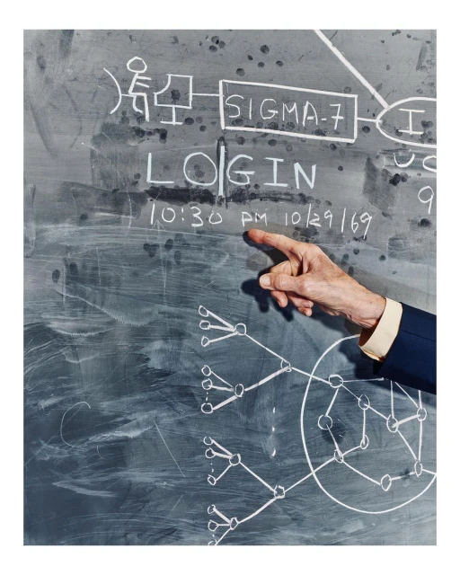 Finger points to chalkboard with white text, diagrams, and the date 10/29/69, in a close-up shot with a shallow depth of field.