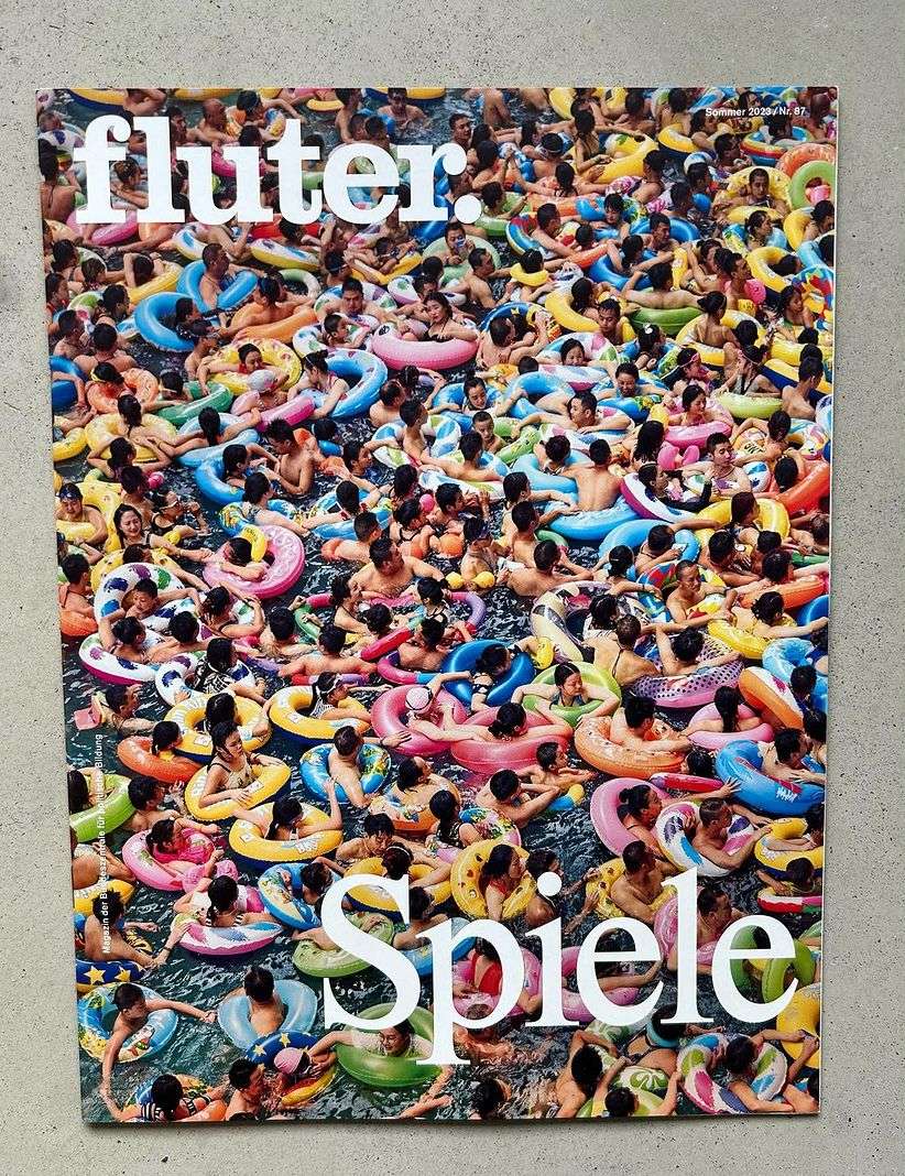 Magazine cover featuring a large group of people in colorful inflatable tubes floating in a body of water, taken from an overhead angle.