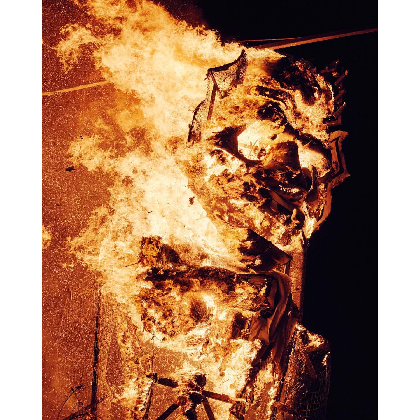 Abstract depiction of a structure engulfed in flames with an orange glow dominating the scene against a black background.