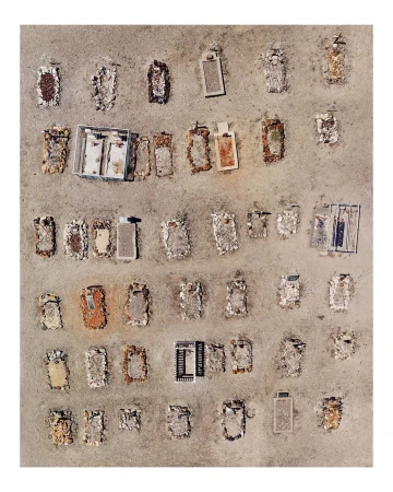 Aerial photograph of tombstones on sandy ground with varying states of deterioration, stone markers, and a scale reference object.