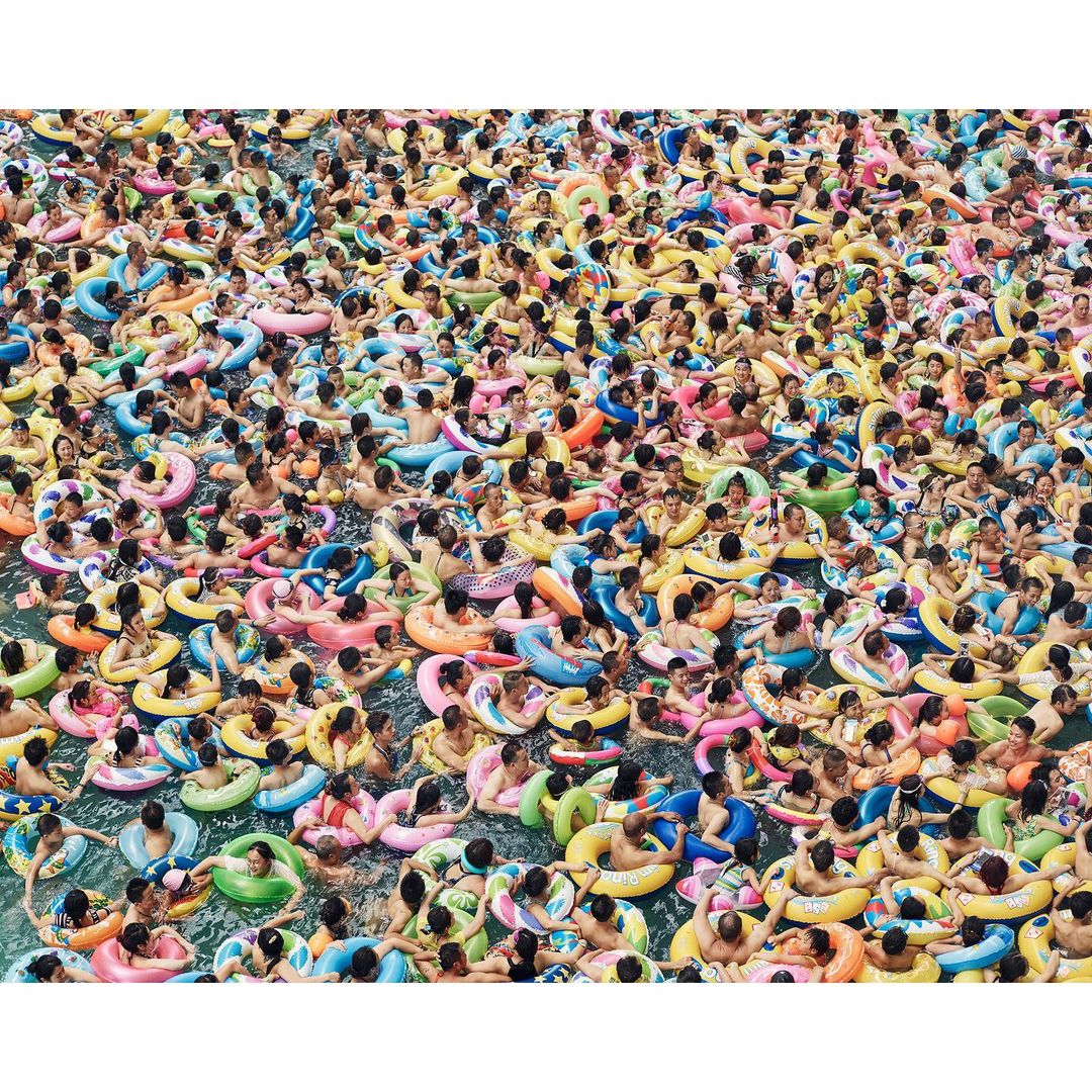 Aerial view of a crowded swimming pool with many people in colourful inflatable rings, creating a vibrant and busy summer scene.