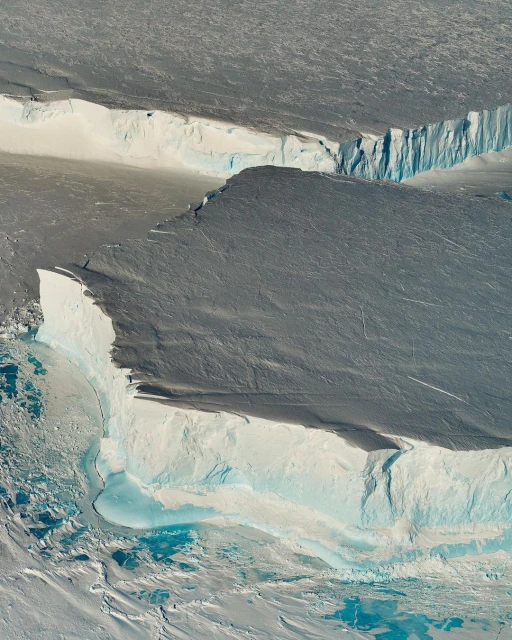 Aerial view of a large glacier showing layers of snow and ice, with a mix of blue, white, and grey coloring the natural landscape.