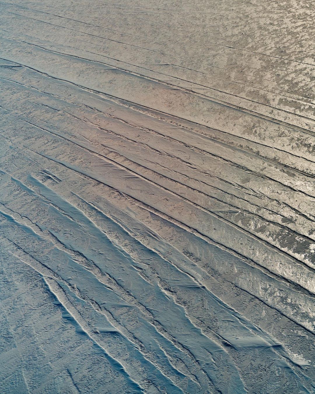 Textured surface with parallel indentations and a subtle gradient from beige to blue, creating an abstract industrial or natural pattern.