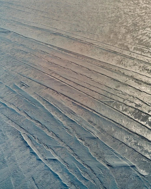 Textured surface with parallel indentations and a subtle gradient from beige to blue, creating an abstract industrial or natural pattern.
