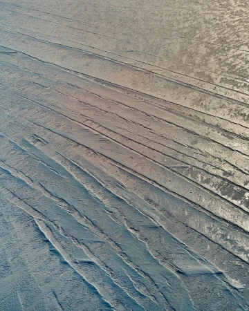 Textured surface with parallel indentations and a subtle gradient from beige to blue, creating an abstract industrial or natural pattern.
