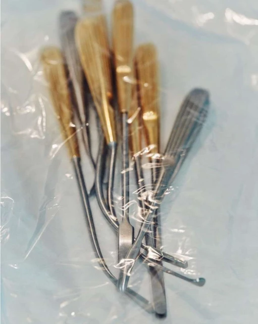 Several metal surgical tools with wooden handles are displayed in a sterile plastic bag, ready for a medical procedure.
