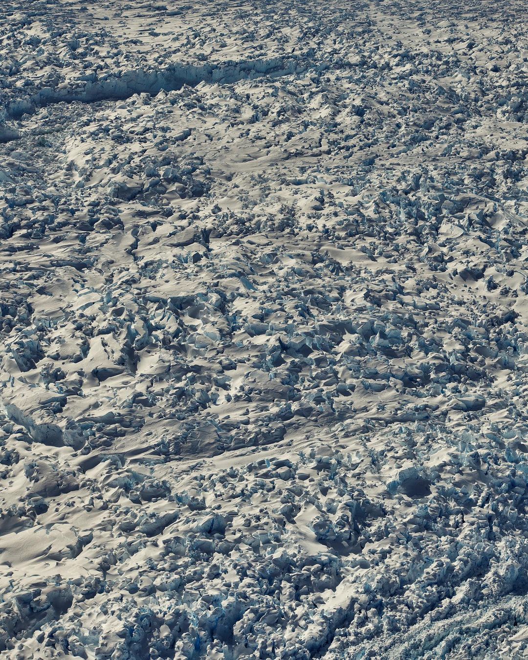 Scenic overhead view of a vast, rugged glacier with deep crevices and icy formations, showing the raw beauty and scale of nature.