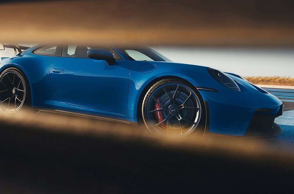 A blue Porsche 911 GT3 car is shown in a low-angle shot on a racetrack, highlighting its aerodynamic design and sporty features.