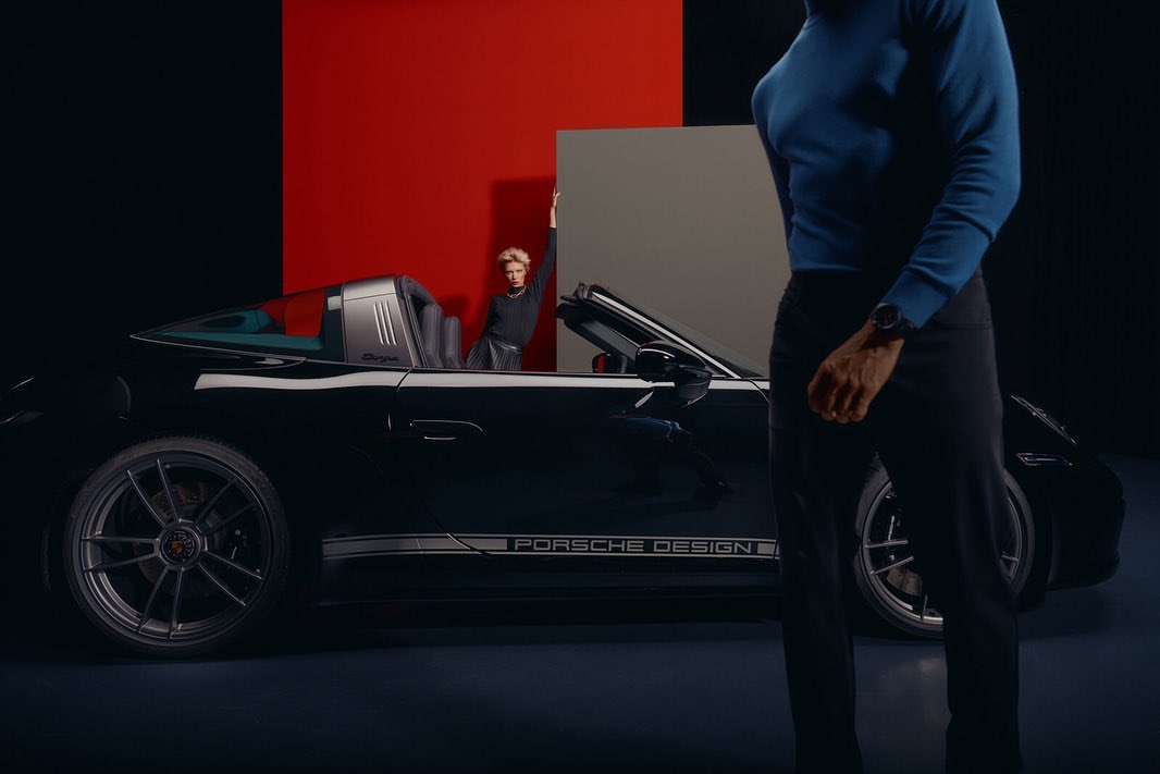 Black Porsche Design Targa convertible car shown with a woman posing inside the car and a man standing in front of the car.