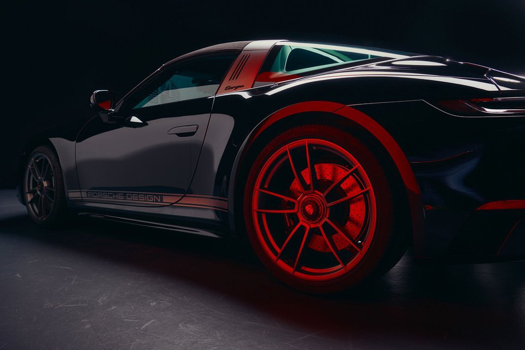 Sleek black Porsche Targa Design edition car with red wheels shown in a dramatic low-angle studio shot with stark rim lighting.
