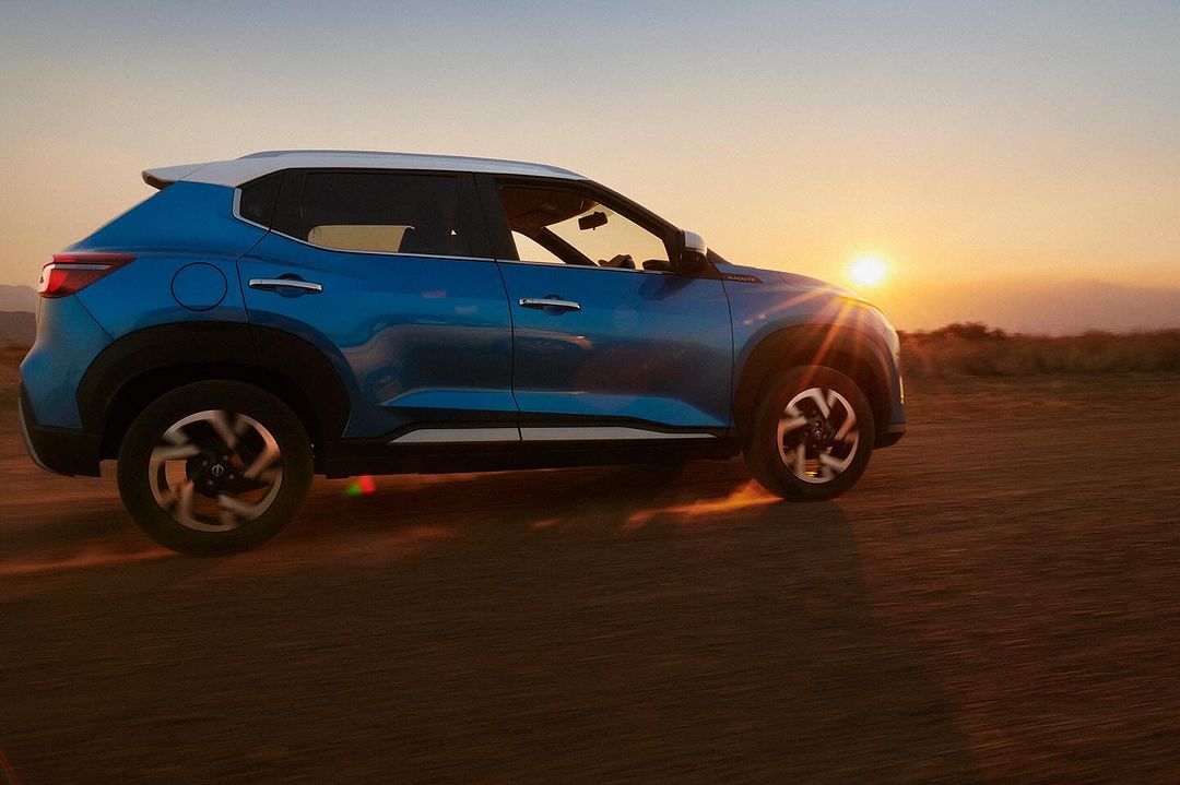 Blue Nissan SUV drives on dirt road during golden hour. The vehicle kicks up dust in the scenic outdoor setting at sunset.