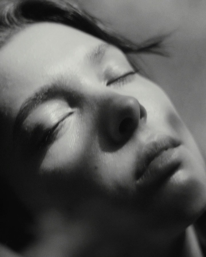 Monochrome close-up portrait of a fair-skinned adult female with closed eyes, featuring soft lighting and a shallow depth of field.