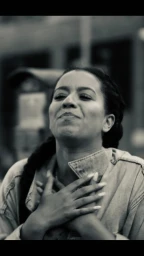 Close-up of a smiling woman with braided hair holding her hands to her chest wearing a denim jacket outdoors.