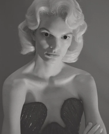 Portrait of a model with sculpted blonde hair and dark voids for eyes, wearing a dark strapless dress, by photographer Till Janz.