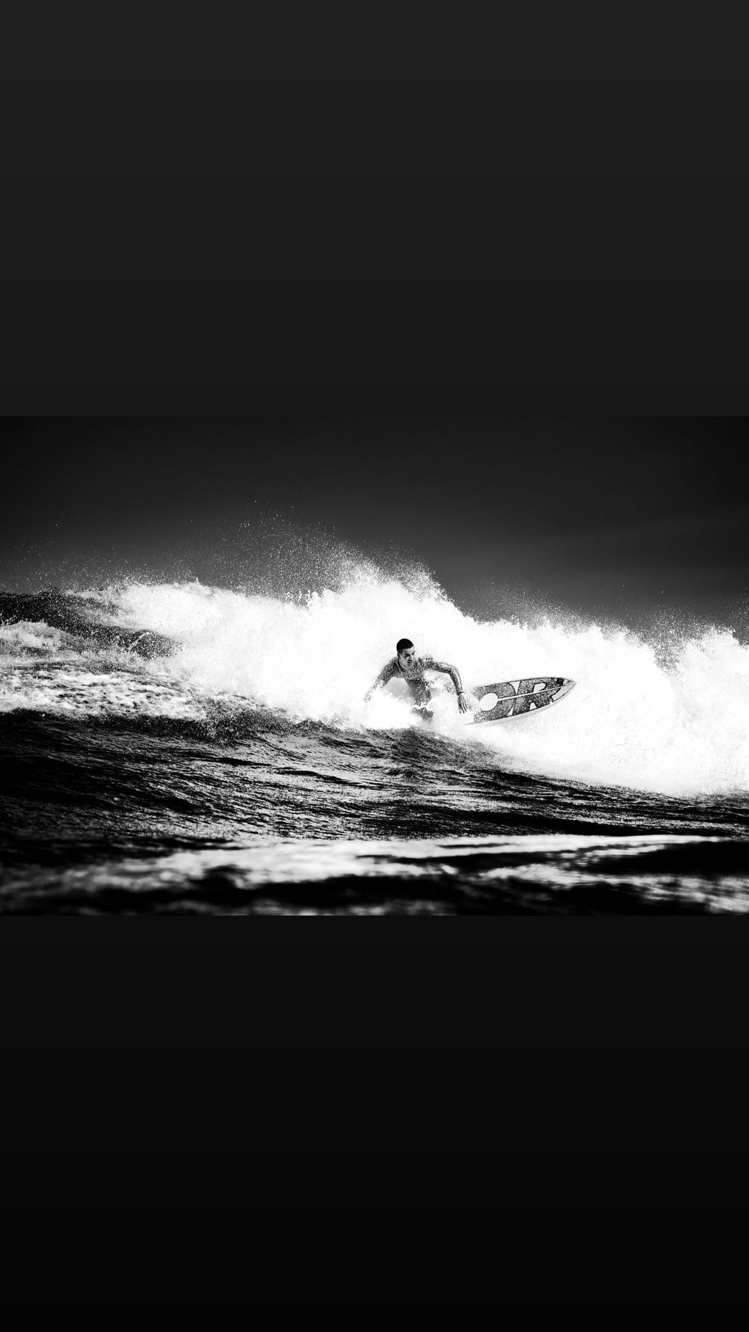Monochrome action shot of an adult surfer riding a wave on a surfboard. Water splashes around him as he navigates the ocean.