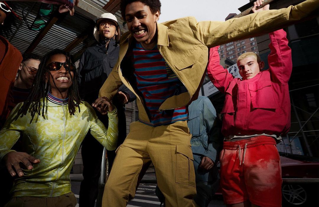 Group of young adults in colorful jackets and pants gathering on an urban sidewalk on a sunny day. Fashion and lifestyle.