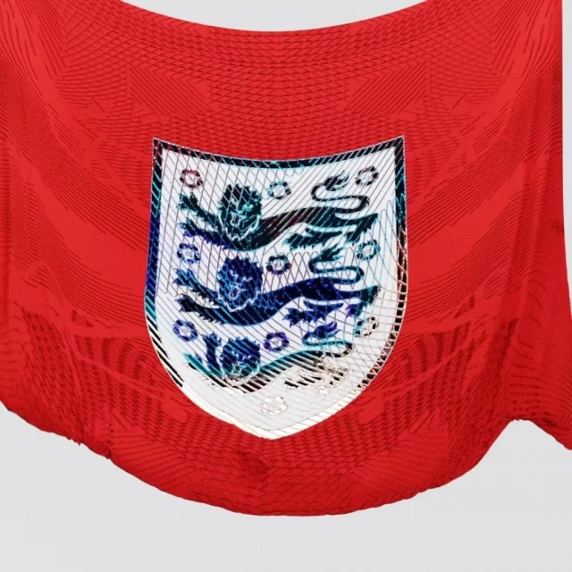 Close-up of a red soccer jersey with a shield emblem featuring three lions, set against a plain background.