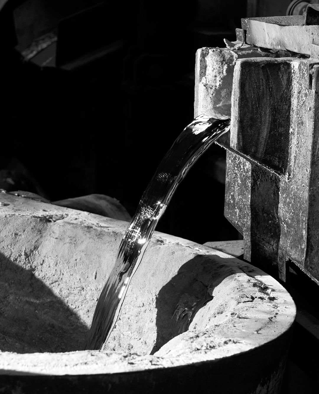 Striking black and white shot of molten metal pouring from a channel into a receptacle, showcasing industrial processes and texture.