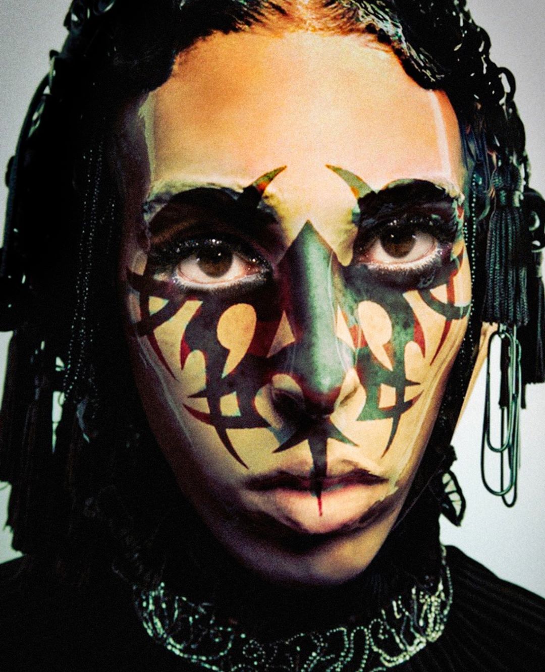 Close-up portrait of a person with tribal face paint, intricate headwear, and decorative jewelry, conveying a bold and artistic aesthetic.
