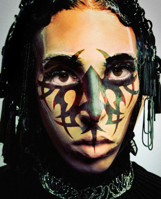Close-up portrait of a person with tribal face paint, intricate headwear, and decorative jewelry, conveying a bold and artistic aesthetic.
