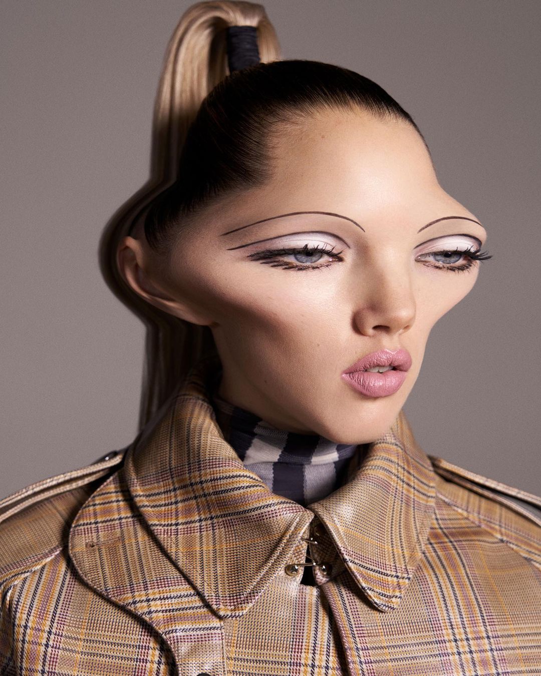 A woman with a high ponytail, wearing a plaid jacket, strikes a pose in a studio, featuring creative makeup and a neutral background.