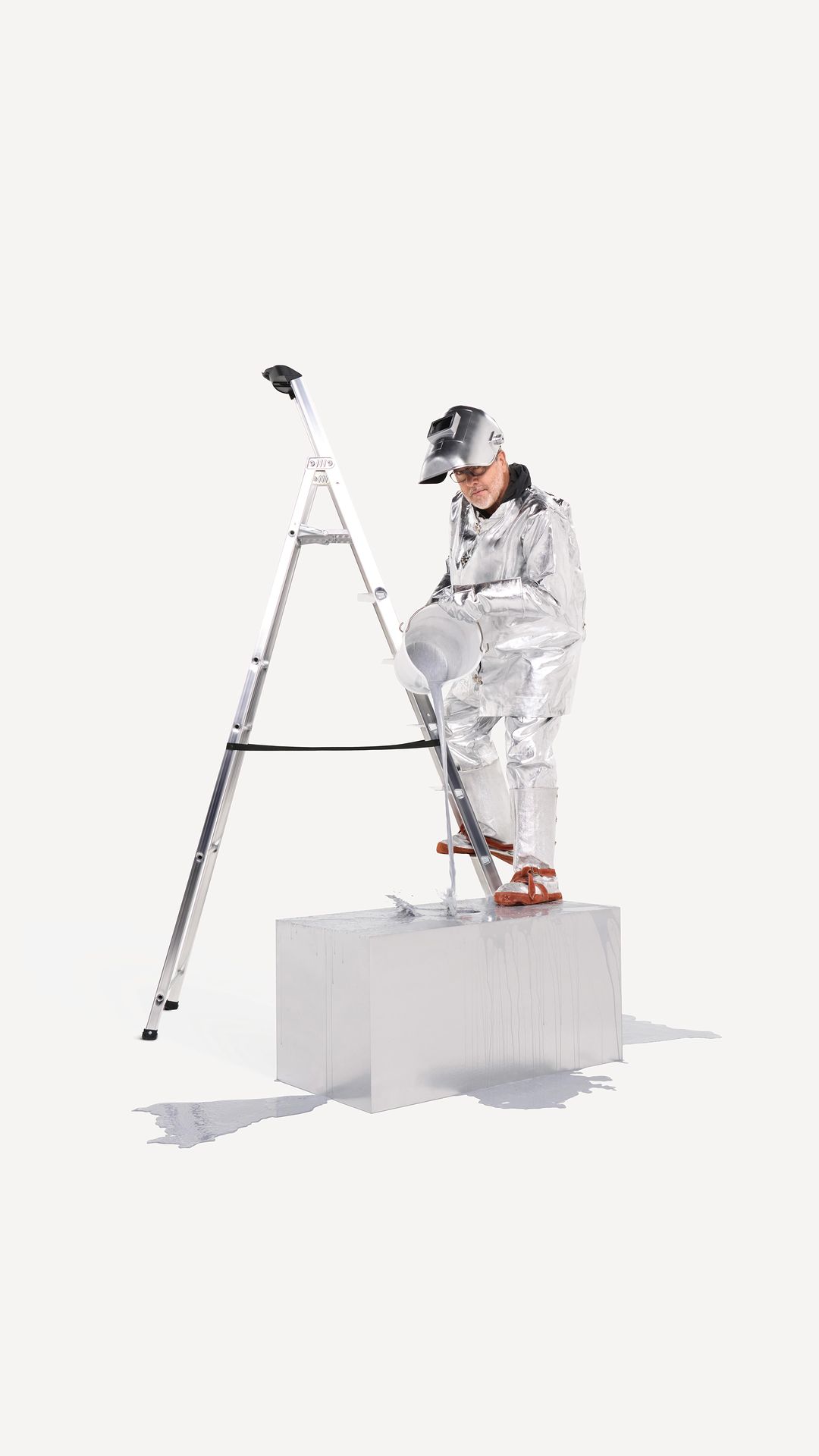 A person in a silver suit standing on a white block next to a ladder against a bright white seamless backdrop in a studio setting.