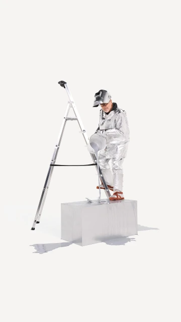 A person in a silver suit standing on a white block next to a ladder against a bright white seamless backdrop in a studio setting.