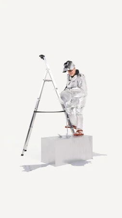 A person in a silver suit standing on a white block next to a ladder against a bright white seamless backdrop in a studio setting.
