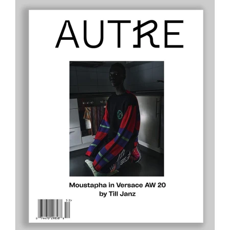 Magazine cover featuring a portrait of a model kneeling in a dark interior space wearing a colourful patterned sweater