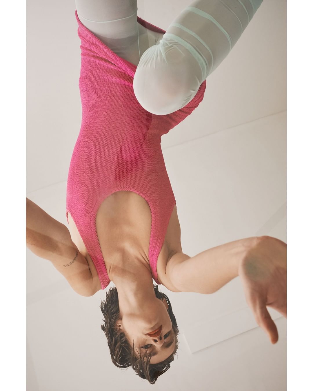 Upside-down view of a slender person in a pink bodysuit and sheer tights, on a white surface. Fashion, style, and artistic expression.