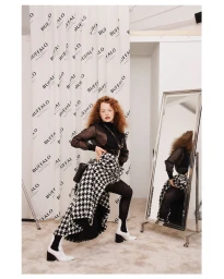 Red-haired model in sheer black top and houndstooth skirt posing by a standing mirror, photographed by Till Janz.
