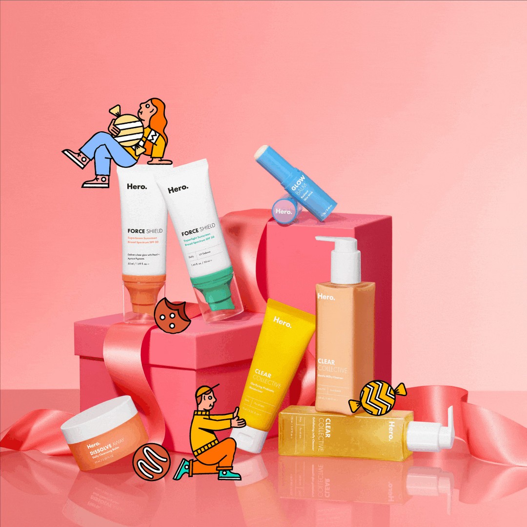 Hero skincare products arranged on a pink gift box with ribbon, featuring tubes, jars, and bottles in a beauty product still life.
