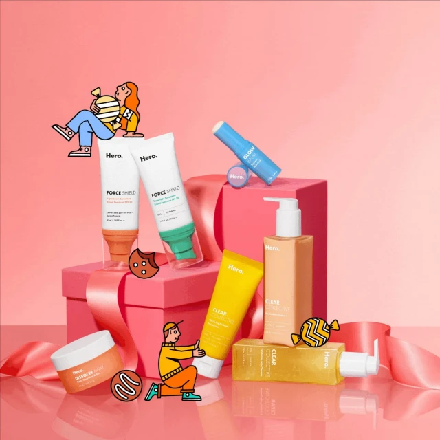 Hero skincare products arranged on a pink gift box with ribbon, featuring tubes, jars, and bottles in a beauty product still life.