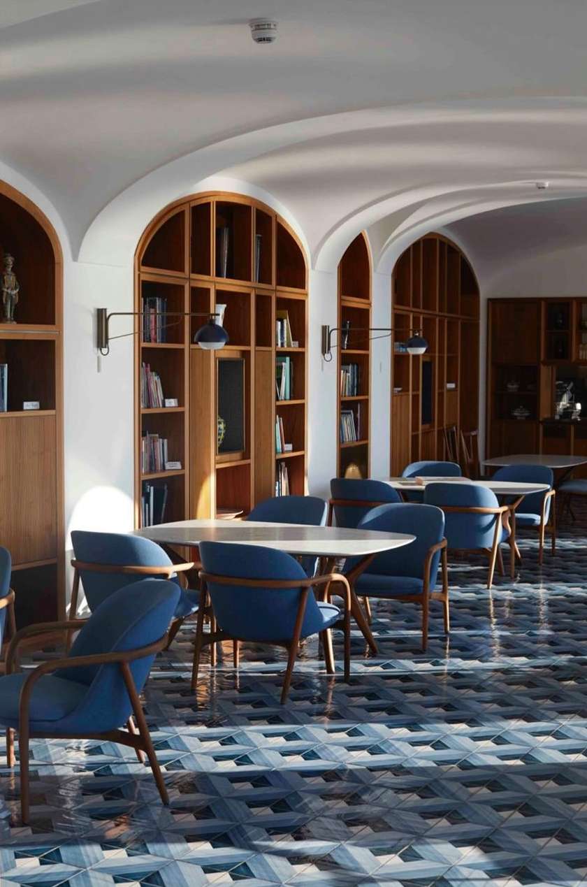Interior view of an architecturally detailed room with light-wood bookshelves, blue chairs, and geometric tile flooring.