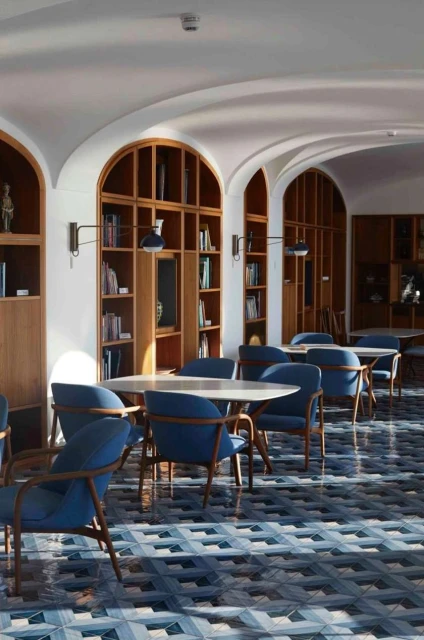 Interior view of an architecturally detailed room with light-wood bookshelves, blue chairs, and geometric tile flooring.