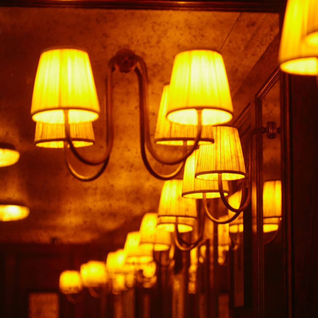 Interior lighting features a line of sconces with fabric lampshades, casting a warm, intimate glow in an indoor setting.