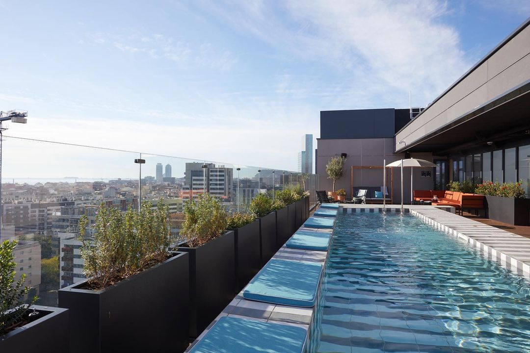 Rooftop pool with city view featuring planters, lounge chairs, and clear skies providing a luxury urban oasis for relaxation.