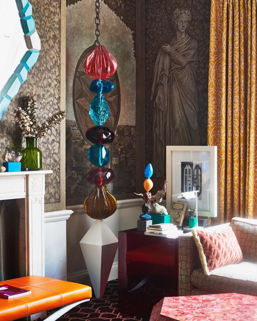 Eclectic interior with a hanging glass sculpture, patterned wallpaper, and bright furniture accents in an elegant residential space.