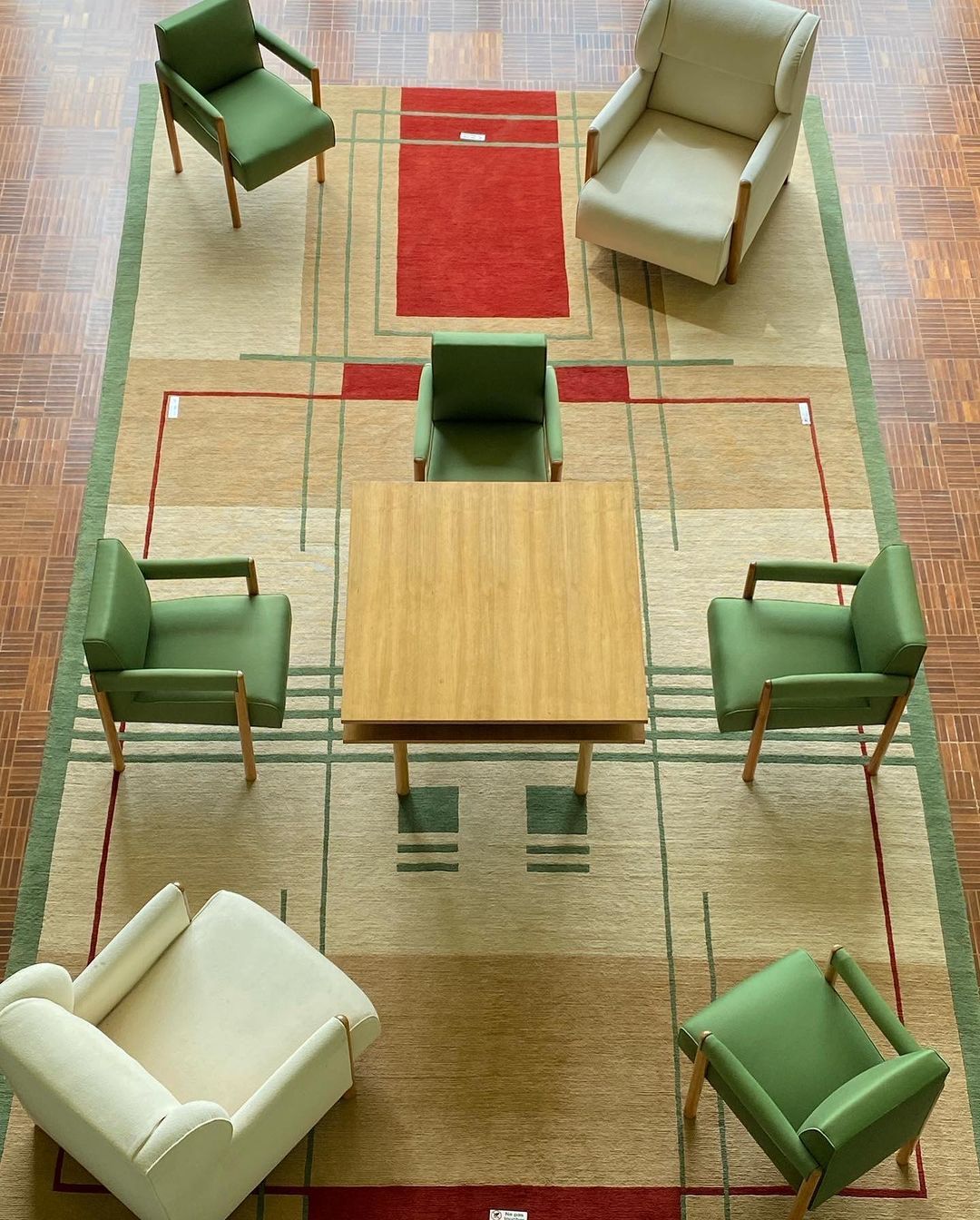 Overhead shot of six chairs arranged around a square wooden table on a patterned rug in an indoor setting; interior design.
