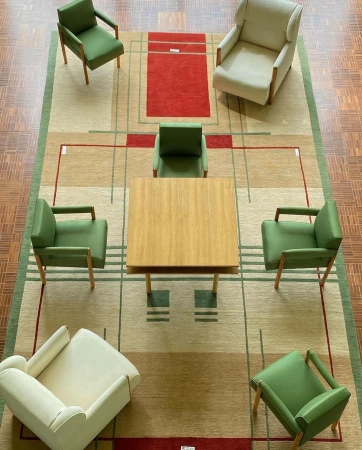 Overhead shot of six chairs arranged around a square wooden table on a patterned rug in an indoor setting; interior design.