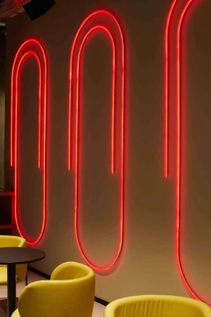 Interior shot of a modern restaurant with yellow chairs and neon paper clip art wall decorations, creating a contemporary ambiance.