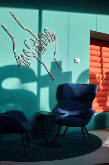 Modern interior features blue armchairs, round table on a blue round rug, and decorative metal hands wall art on a teal wall.