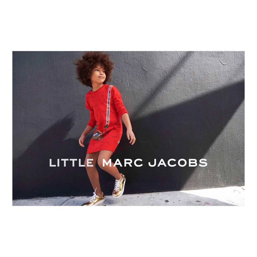 A child model poses dynamically in a red dress and gold sneakers in front of a dark wall, showcasing the LITTLE MARC JACOBS brand.